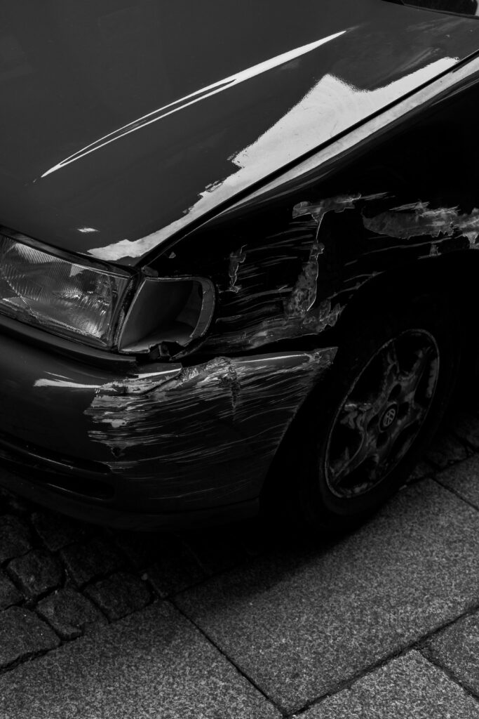 Artistic black and white image of a scratched car fender parked on a cobblestone sidewalk in Porto.